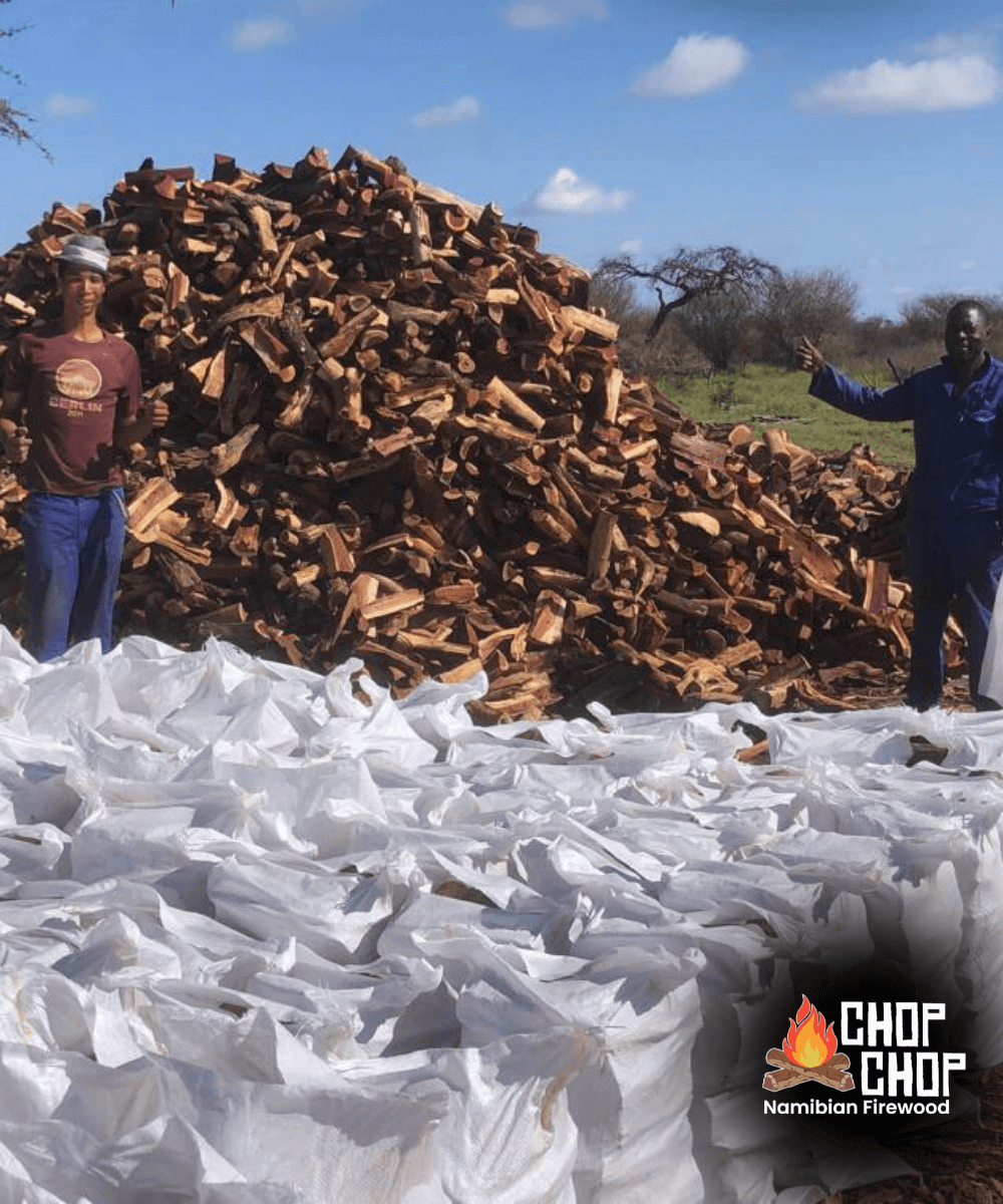 Two individuals showing a pile of Kameeldoring Kindling Firestarter bags and stacked firewood.